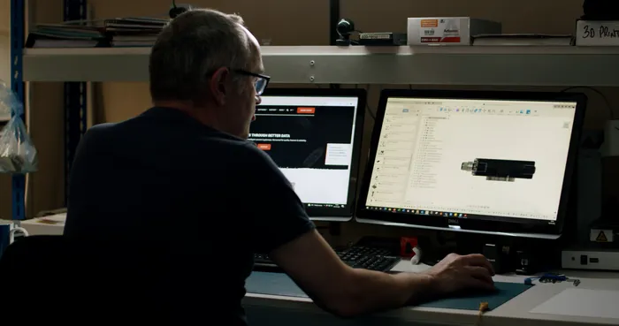 A man working on a dual screen computer in the dark.