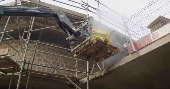 A cherry picker lifting materials onto the roof of a construction site.