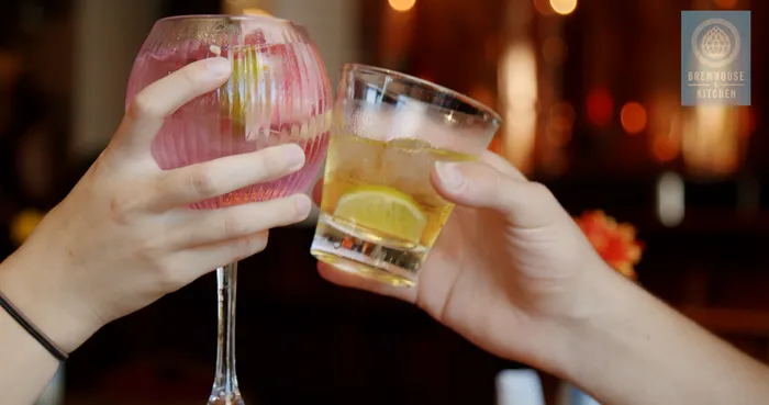 A closeup of a glass of pink gin and another glass of lemon vodka being clinked together by two hand