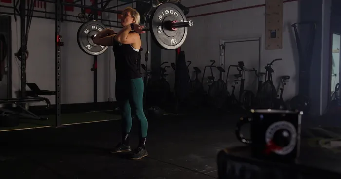 A female weightlifter in green leggings lifting an Olympic barbell.