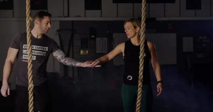 A male and female athlete stood in front of two climbing ropes suspended from the ceiling.