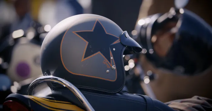 A grey open face motorbike helmet with black star artwork ontop of a motorbike seat.