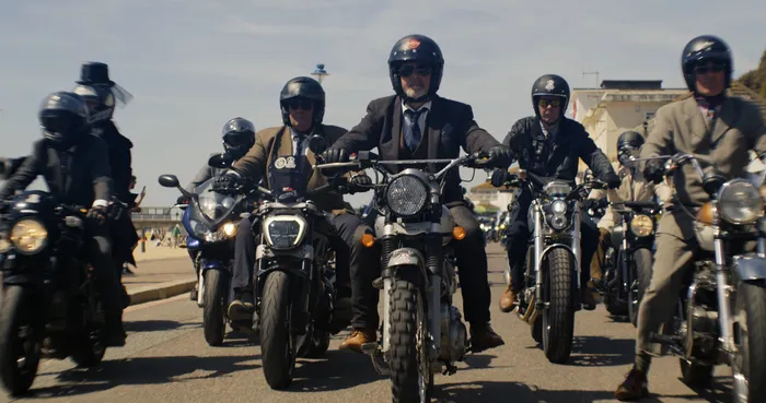 Six motorcyclists wearing formal suits driving towards the camera on Poole Quay.